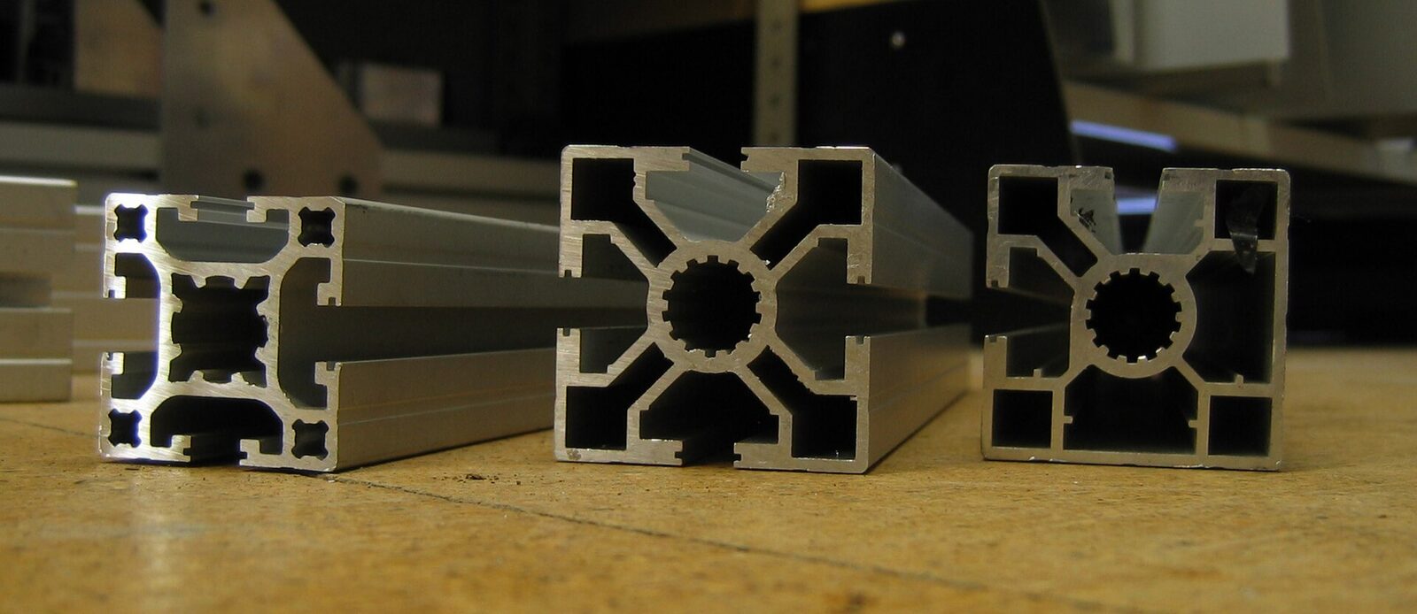 Three T-slot aluminum extrusion profiles standing on end, showing their cross-sections